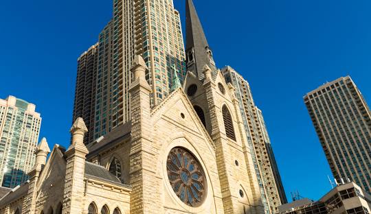 A view of Chicago's Holy Name Cathedral including the steeple and portions of the city skyline.  The churches beautiful stained glass rose window can be seen for blocks.